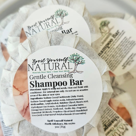 Multiple shampoo bars wrapped in individual paper wrappers, placed on a white plate with a soft, textured background.