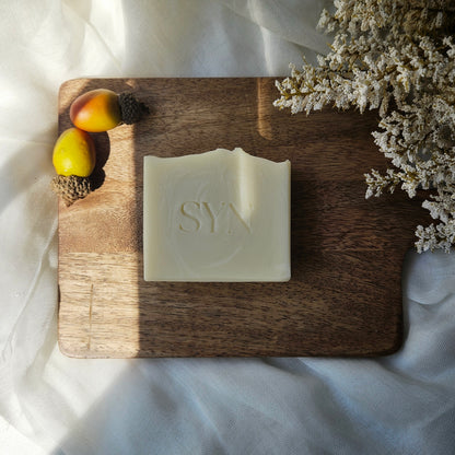 Bar of soap with 'SY' branding on a wooden cutting board with fruits and flowers.