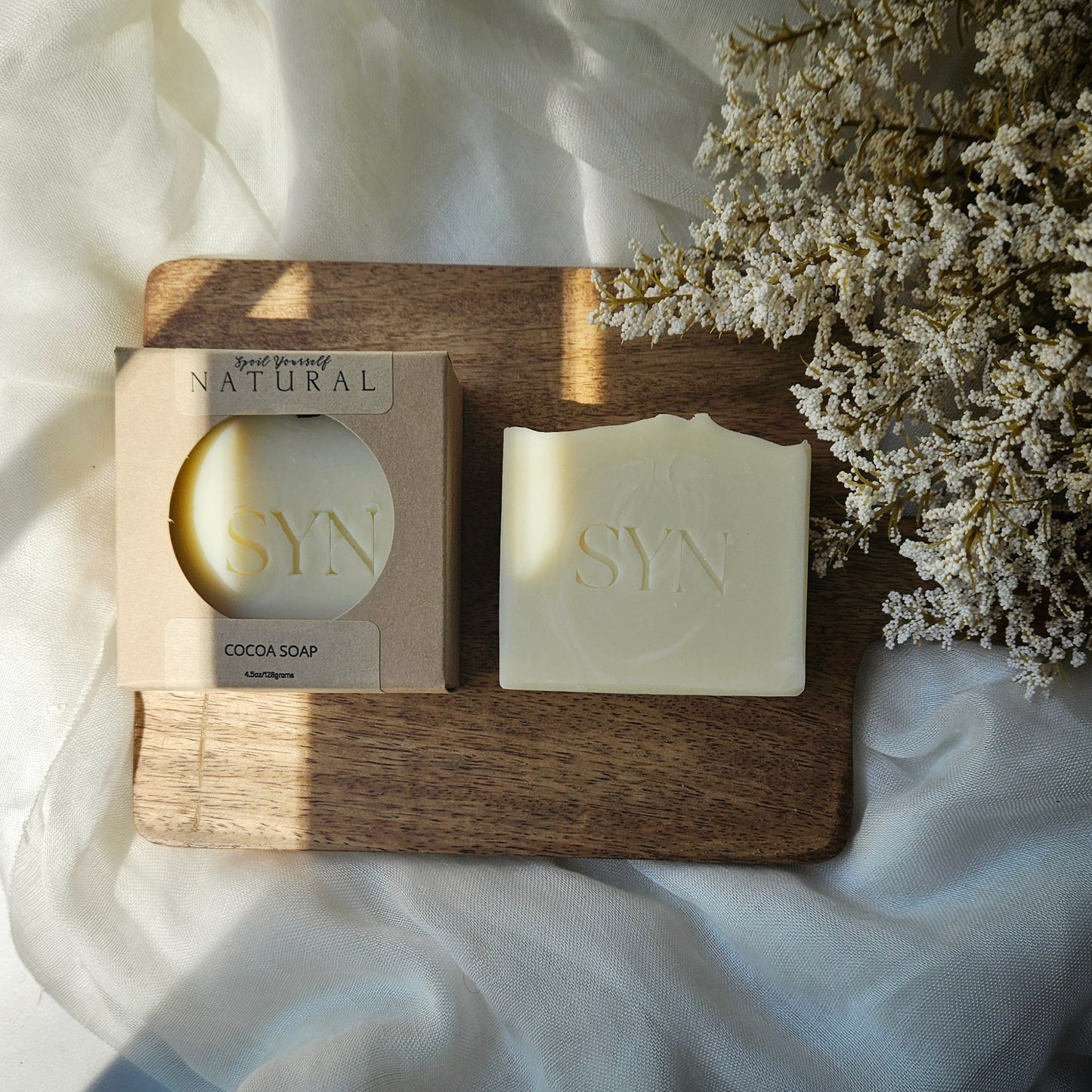 SYN soap bar and packaging on a wooden board with dried flowers