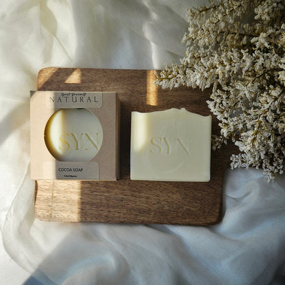 SYN soap bar and packaging on a wooden board with dried flowers