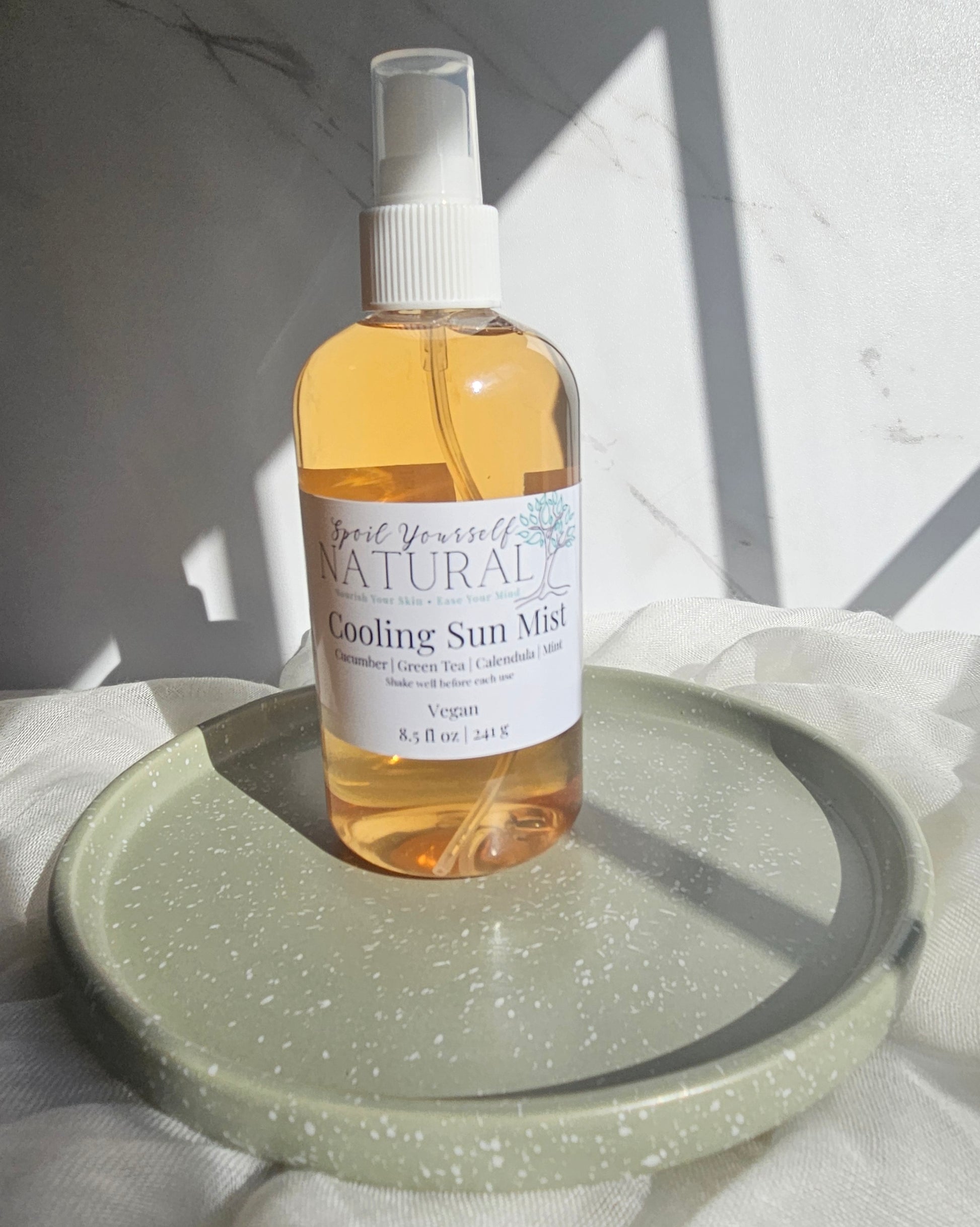Bottle of 'Cooling Sun Mist' on a green plate with a white background