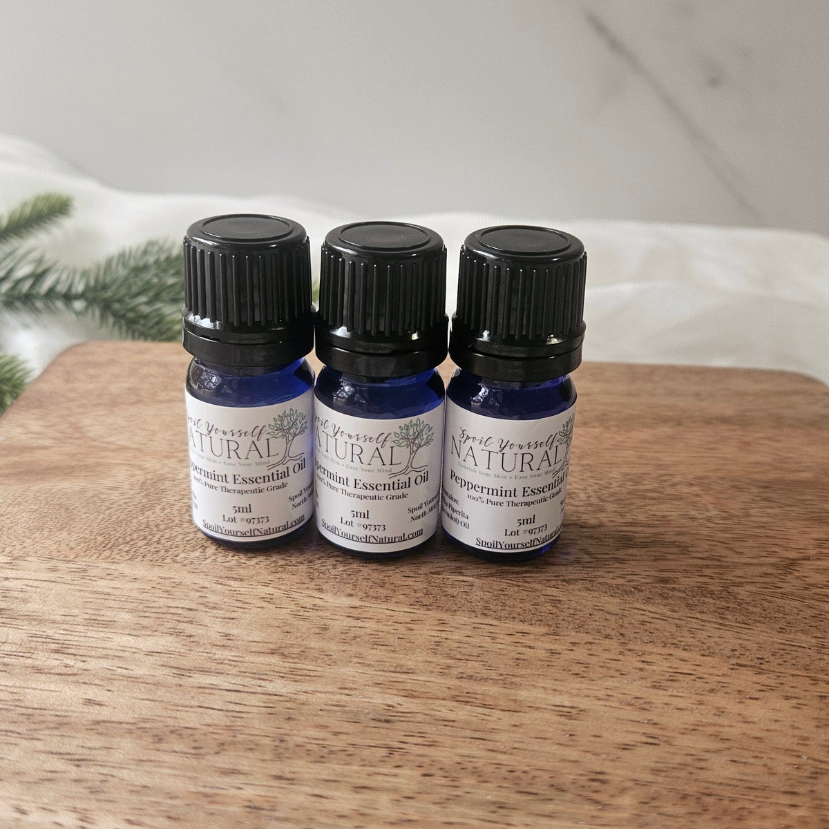 Three bottles of peppermint essential oil on a wooden surface with a white background.