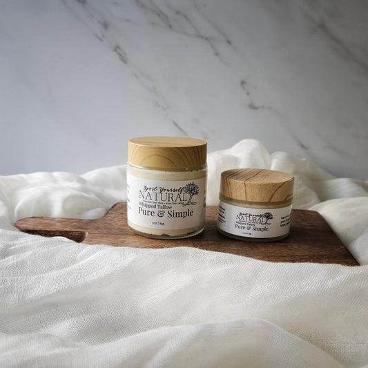 Two containers of whipped tallow balm, one larger and one smaller, with labels that read 'Nature's Pure Simple, Fresh & Simple'. They are placed on a white fabric surface with a marble background.
