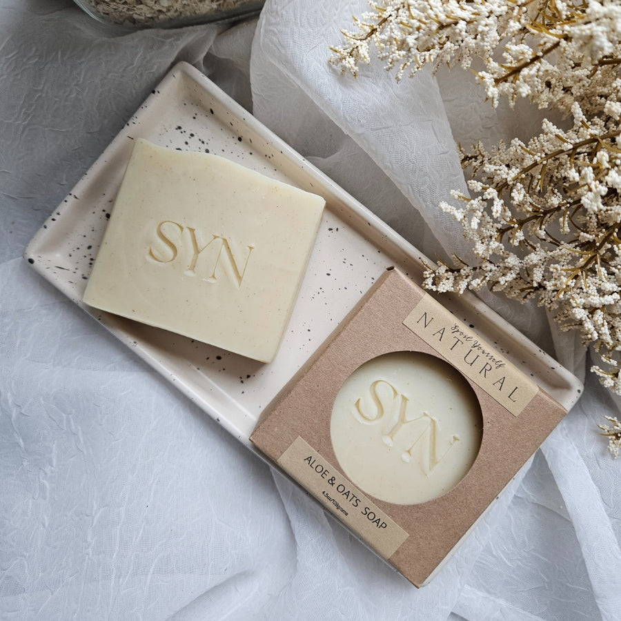 two bars of bar soap, one is boxed and the other is not. there are flowers in the background