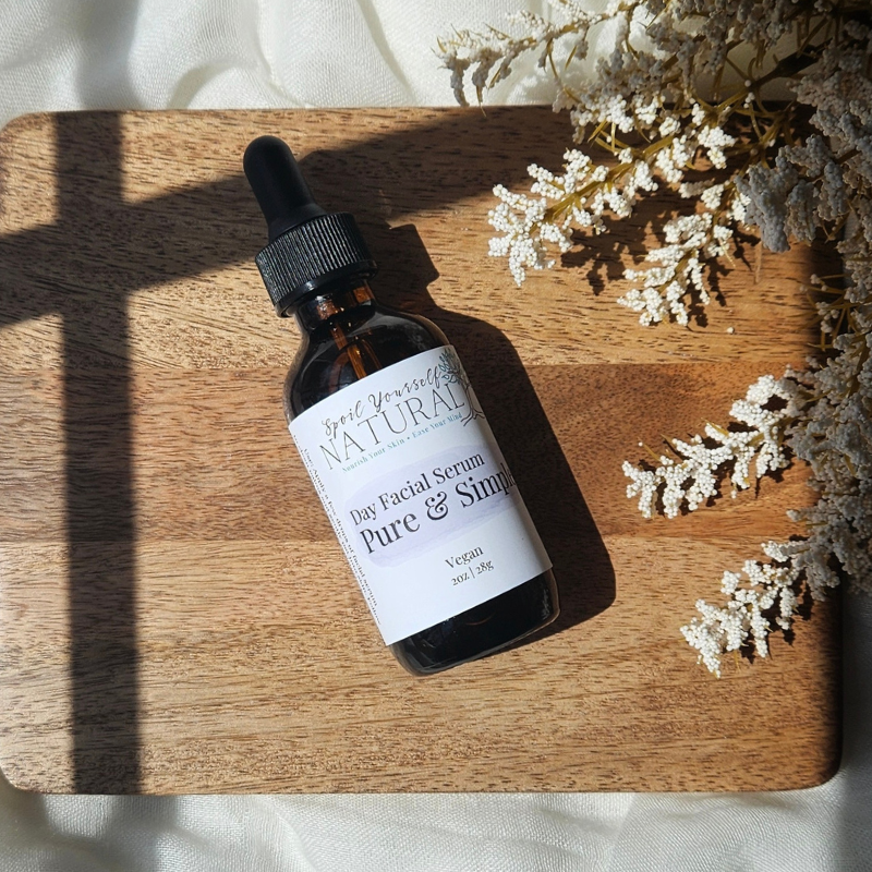 A dropper bottle of Day Facial Serum with squalane, placed on a wooden board with a white flower to the side.