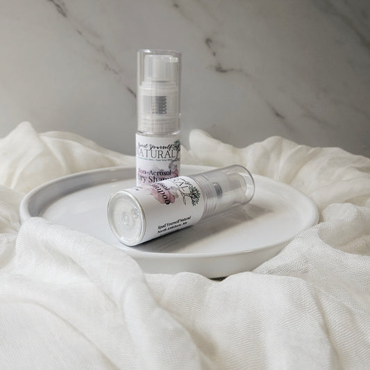 A bottle of non-aerosol dry shampoo placed on a white surface, with a cap beside it, against a marble background.
