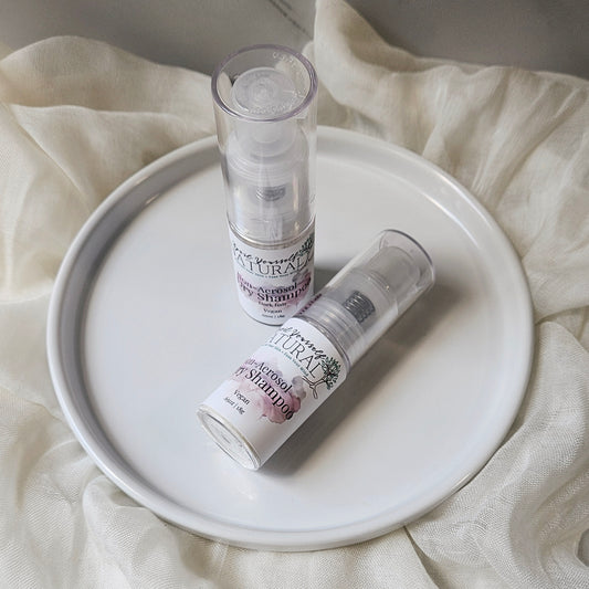 A close up of a  bottle of non-aerosol dry shampoo placed on a white surface, with a cap beside it, against a marble background.