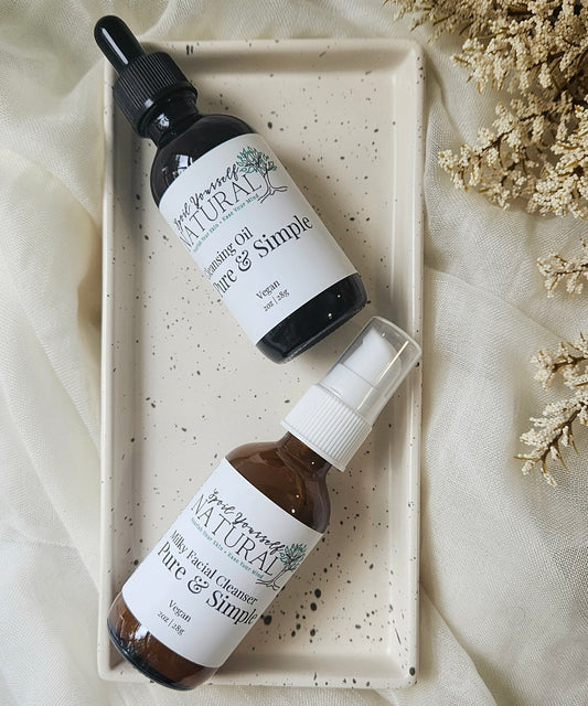 A facial cleansing oil bottle and a milky facial cleanser bottle arranged on a white tray with a neutral background.
