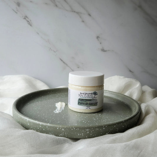 A jar of facial night cream placed on a ceramic plate with a small amount of cream spread out in front of it, all set against a marble background with a neutral color scheme.