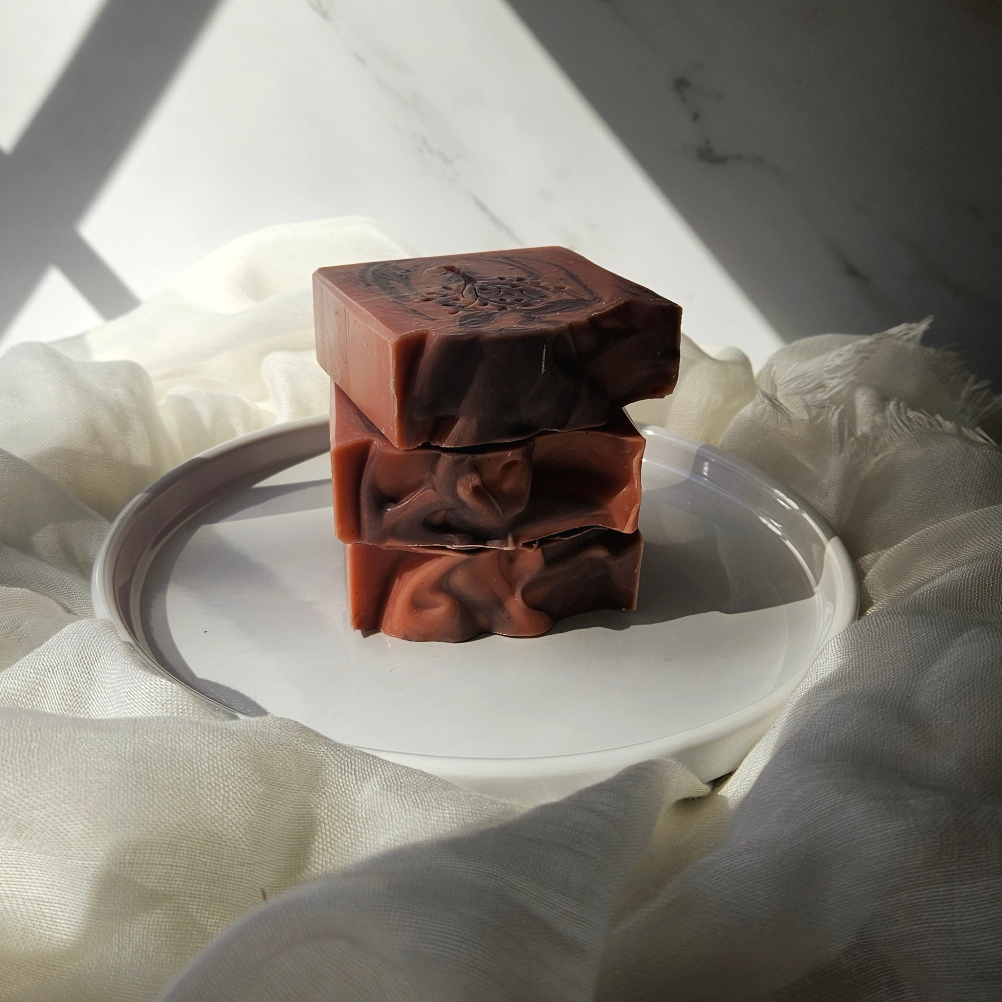 Stack of brown soap bars on a white plate with a white cloth background
