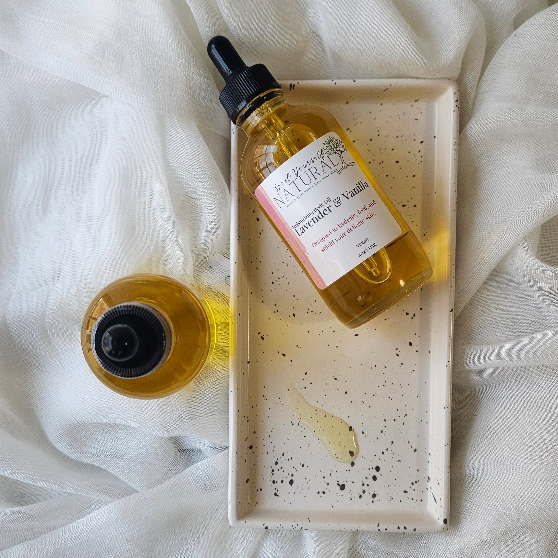 Bottle of lavender and vanilla essential oil with dropper on a speckled tray against a white fabric background