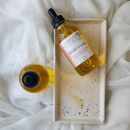 Bottle of lavender and vanilla essential oil with dropper on a speckled tray against a white fabric background