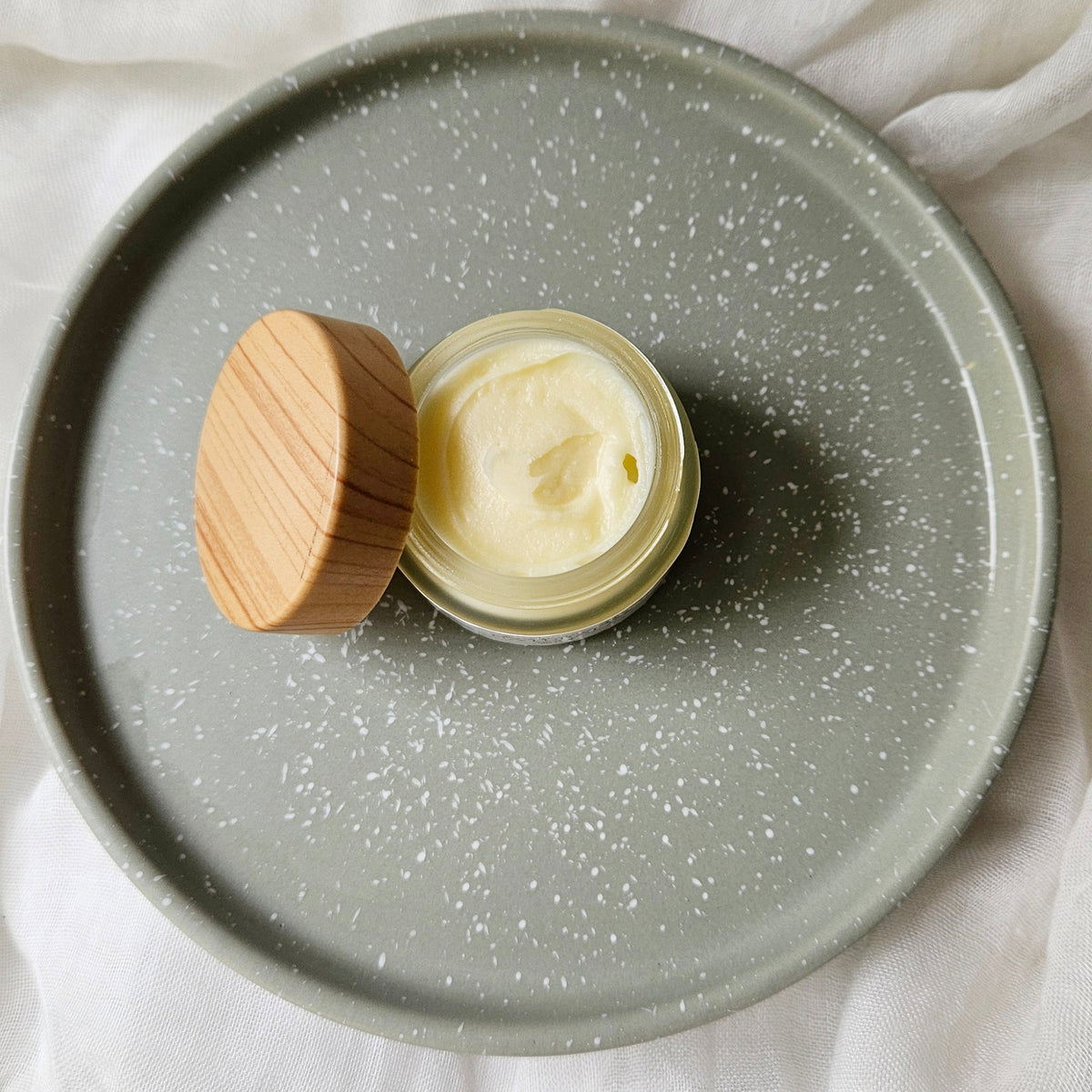 Jar of lip mask with wooden lid on a gray speckled plate