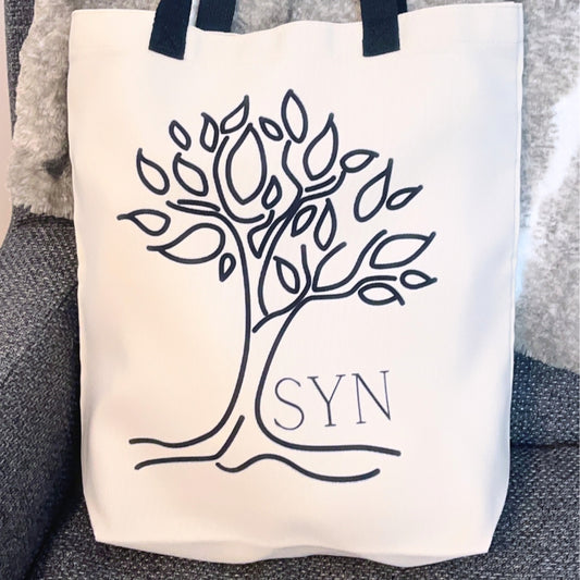 a close ip of the tote bag with the image of a tree in blag that is syns logo