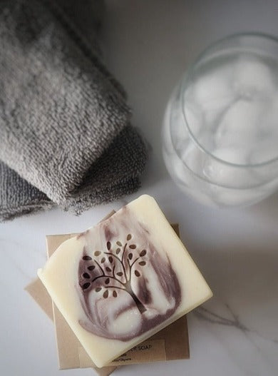bar of lavender soap placed on closed boxes of soaps with a glass of iced water and facial clothes